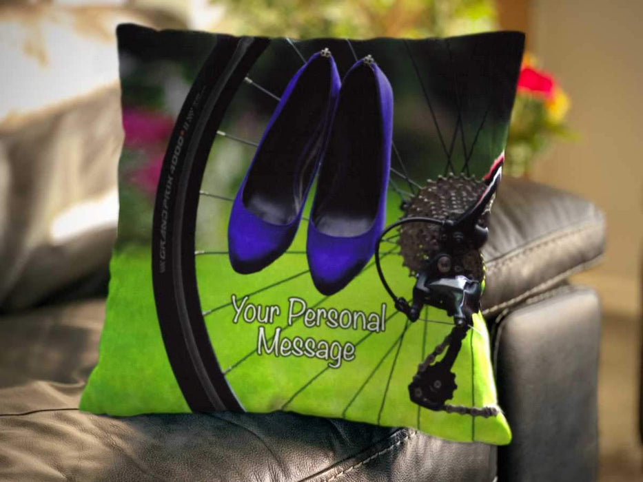 An image of a cushion on a couch, the cushion cover showing an image of a rear wheel of a bicycle with a pair of purple high heel shoes hung over the spokes of the wheel along with a personal message on the cushion