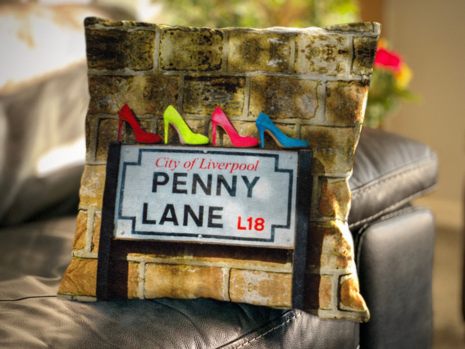 An image of a cushion on a couch, the cushion cover showing the famous penny lane road sign in liverpool, and upon that road sign is four high heeled shoes