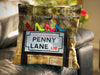 An image of a cushion on a couch, the cushion cover showing the famous penny lane road sign in liverpool, and upon that road sign is four high heeled shoes, there is also a personal message printed on the cushion