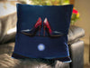 An image of a cushion on a couch, the cushion having an image of a pair of red and blue high heel shoes sat upon the bonet of a car