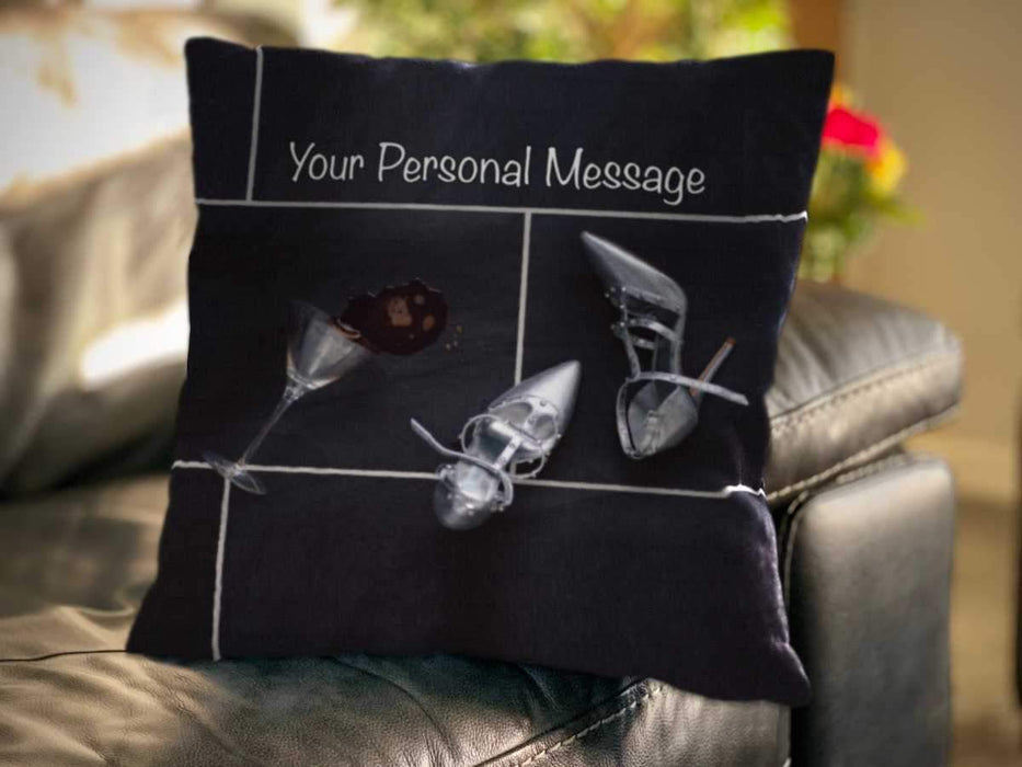 An image of a cushion sat on a couch, the cushion cover showing a cocktail glass on its side with a spilt drink on the floor next to a pair of silver high heel shoes, along with a personal message