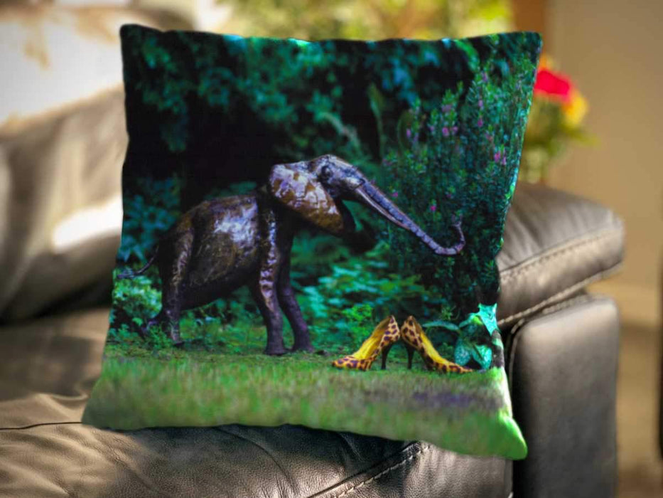 An image of a cushion on a couch, the cushion having a cover showing a pair of yellow high heel shoes sat on grass in a garden along side a metalic elephant