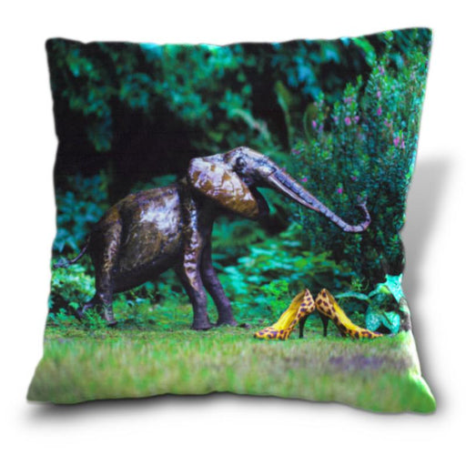 An image of a cushion, the cushion having a cover showing a pair of yellow high heel shoes sat on grass in a garden along side a metalic elephant