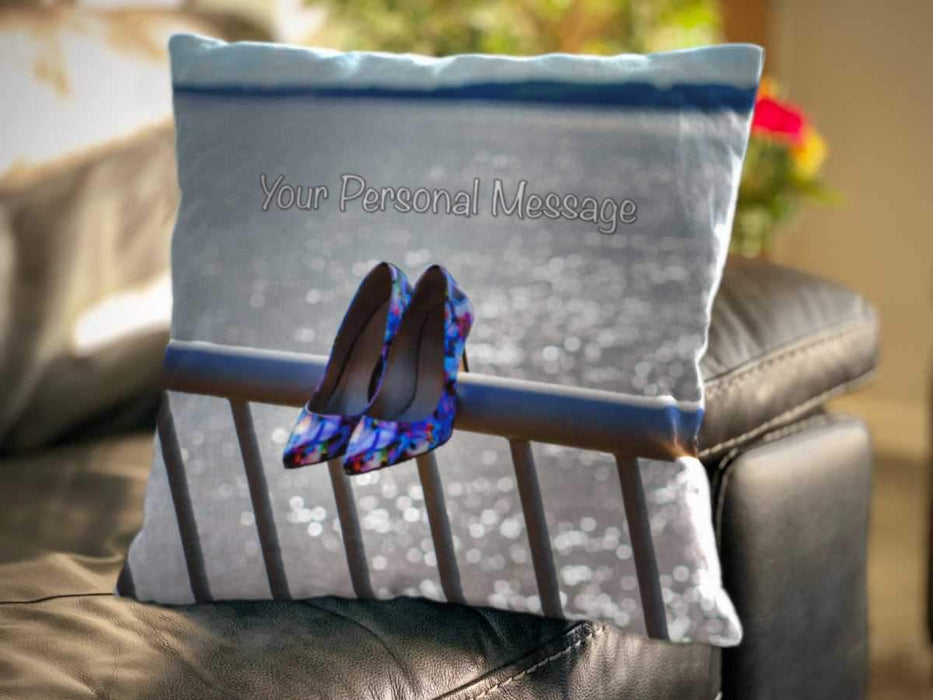 <T>An image of a cushion on a couch, the cushion showing an image of a pair of blue shows hung on the railings adjacent to ocean with the water sparkling behind, along with a personal message on the cushion