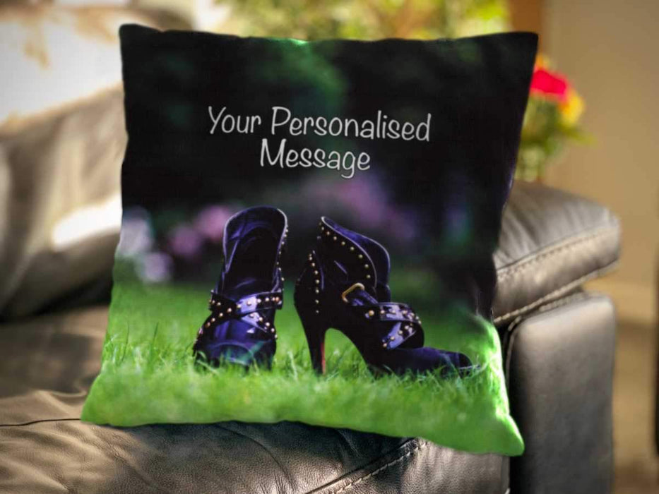 <T>An image of a cushion on a couch, the cushion having a cover showing a pair of purple high heel ankle boots sat upon a garden lawn along with a personal message