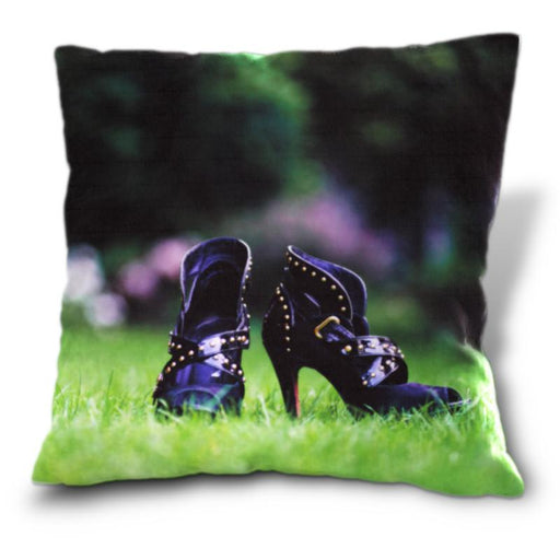 An image of a cushion, the cushion having a cover showing a pair of purple high heel ankle boots sat upon a garden lawn