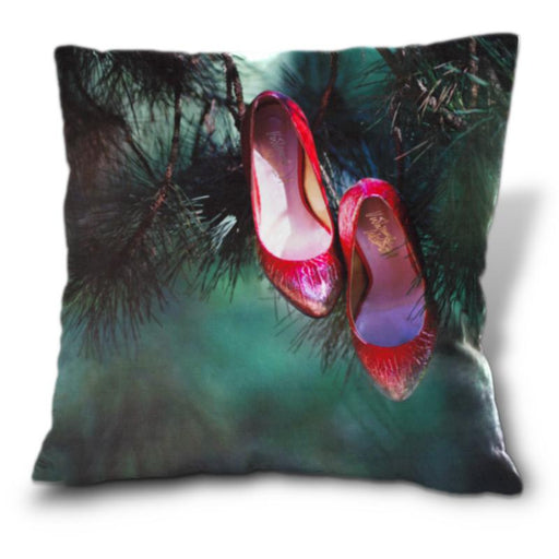 An image of a cushion, the cushion having a cover showing a pair of pink high heel shoes hanging from a tree