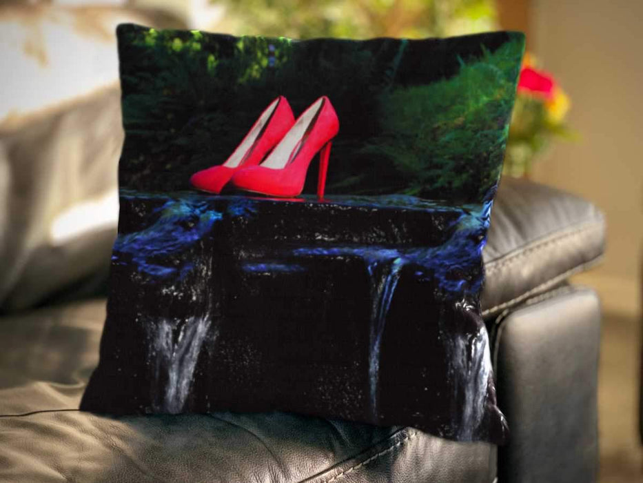 An image of a cushion on a couch, the cushion cover showing an image of a pair of pink high heel shoes sat on a rock in the middle of a flowing river