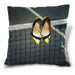 An image of a cushion,, the cushion having a cover showing a pair of yellow high heel shoes hung on a tennis net