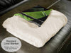 a white fleece blanket folded, with a corner folded towards the viewer showing green and black under the blanket
