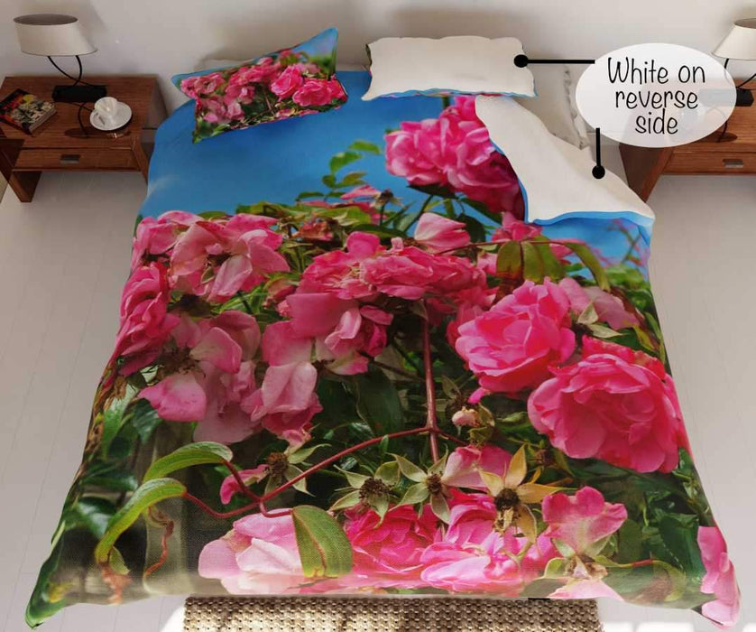 A duvet on a bed, the duvet having a pattern of pink roses with blue sky in the background with a folded corner revealing a white underside