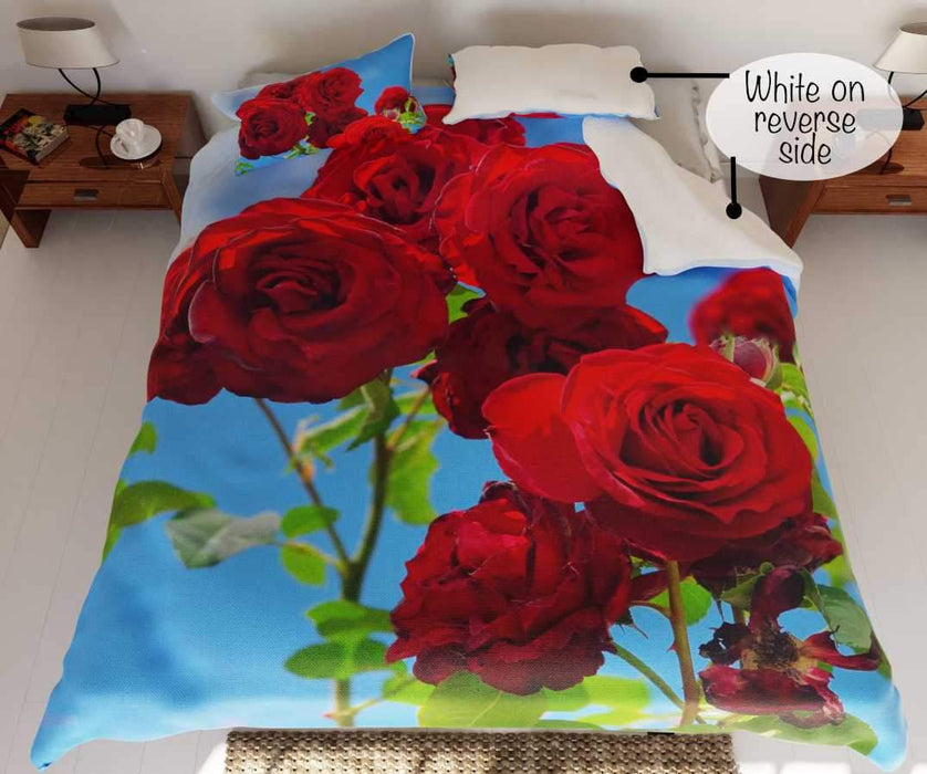 A duvet on a bed, the duvet having a pattern of red roses with blue sky in the background with a folded corner revealing a white underside