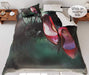 A duvet cover on a bed, the duvet cover having image of a red pair of high heel shoes hung from branch of a tree, a corner of the duvet is folded back to show a white underside