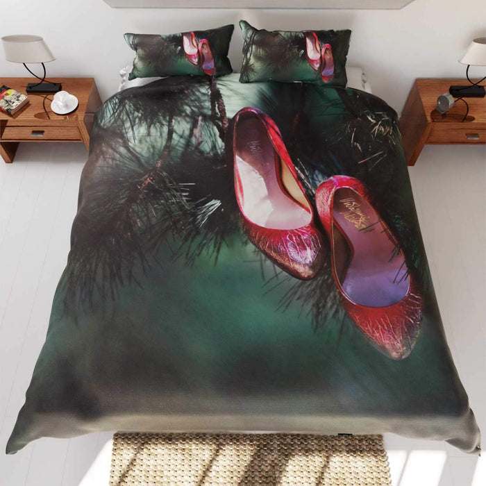 A duvet cover on a bed, the duvet cover having image of a red pair of high heel shoes hung from branch of a tree
