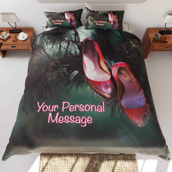 A duvet cover on a bed, the duvet cover having image of a red pair of high heel shoes hung from branch of a tree, along with a personal message on the duvet