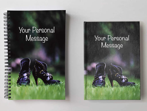 Two notebooks, side by side, both having covers with a close up image of a pair of purple ladies high heel ankle boots in middle of a garden, with a personal message on the cover