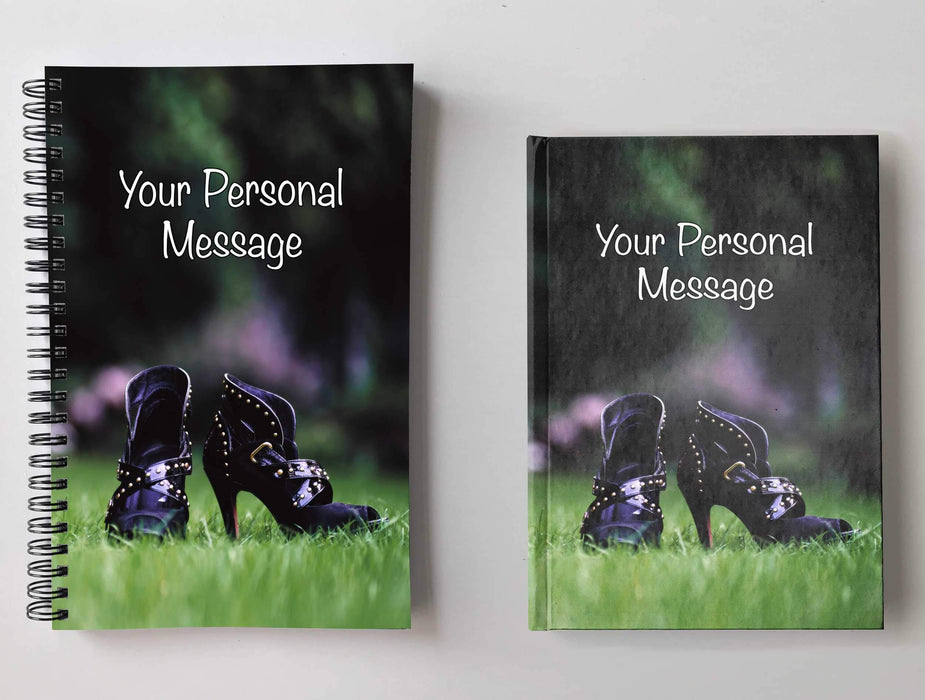 Two notebooks, side by side, both having covers with a close up image of a pair of purple ladies high heel ankle boots in middle of a garden, with a personal message on the cover