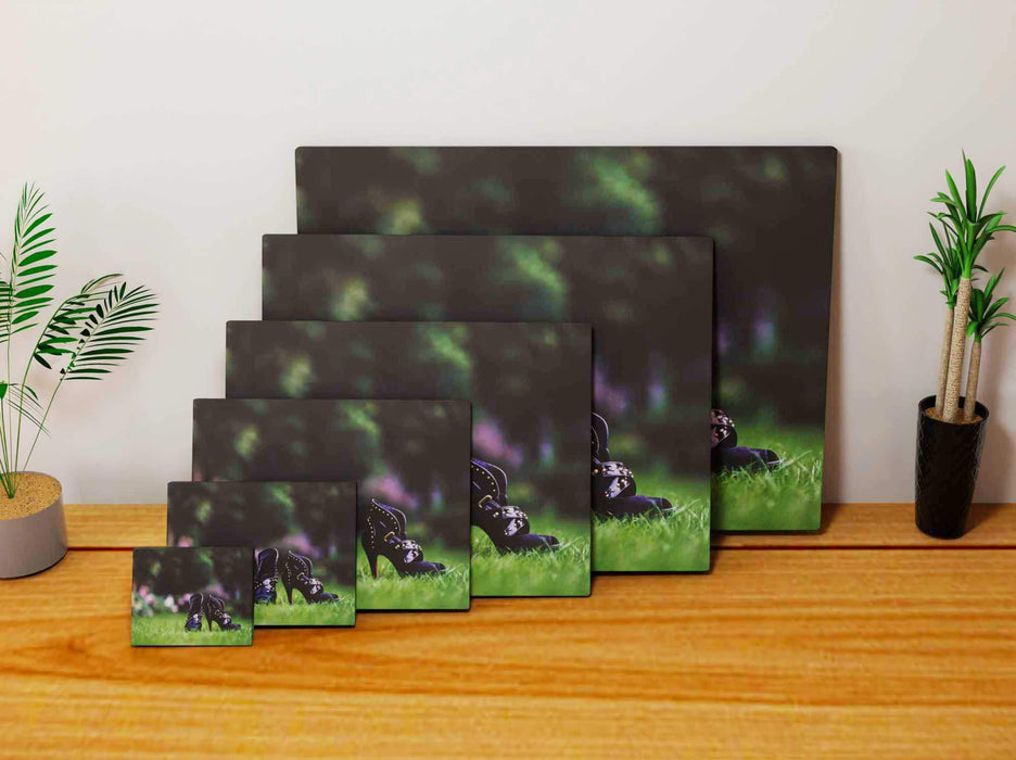 Multiple canvas prints, all of different sizes, each canvas print of a pair of purple high heel shoes stood on grass, the prints are leaning against each other against a wall