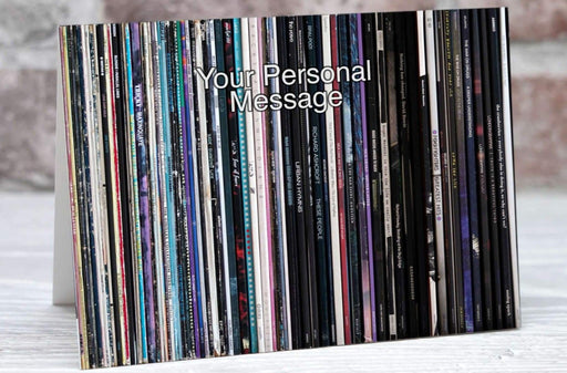 A greeting or birthday card showing a series of vinyl records stacked along a shelf with a personal message on the card, with the card sat adjacent to an envelope and pen