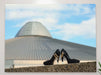 A canvas print of a pair of black high heel shoes sitting on a wall with a building in the background, the building has a slight UFO look to it