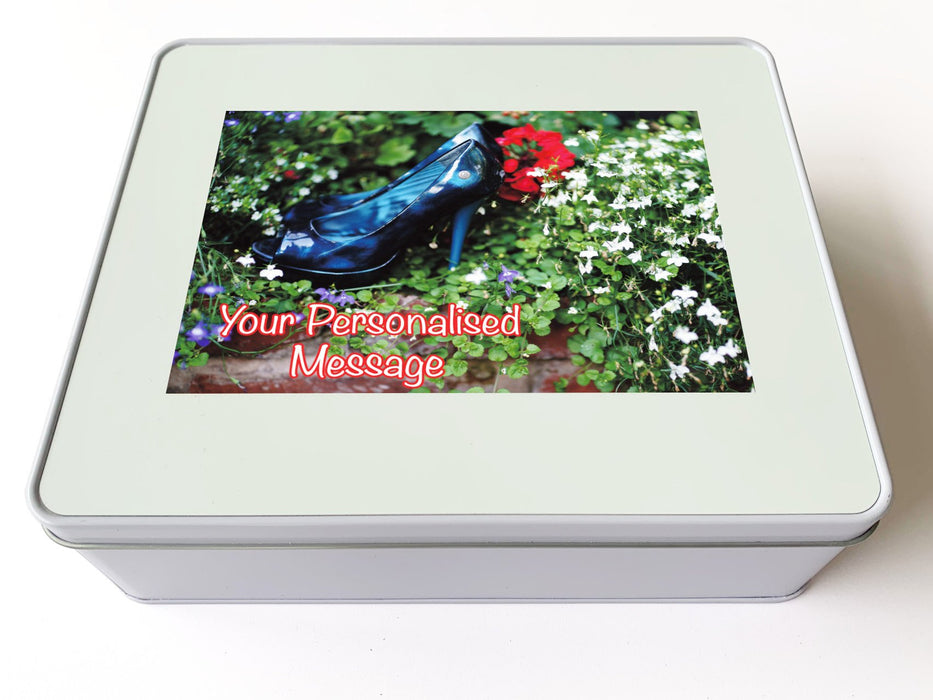 A white tin box, and there is an image on the box of a pair of blue shoes in a flower bed