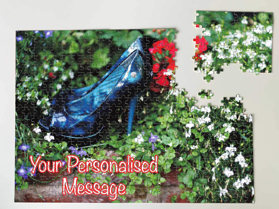 A jigsaw seen from the top, the jigsaw having an image of a pair of blue shoes sitting in a flower bed along with a personal message, the jigsaw is broken into a few pieces