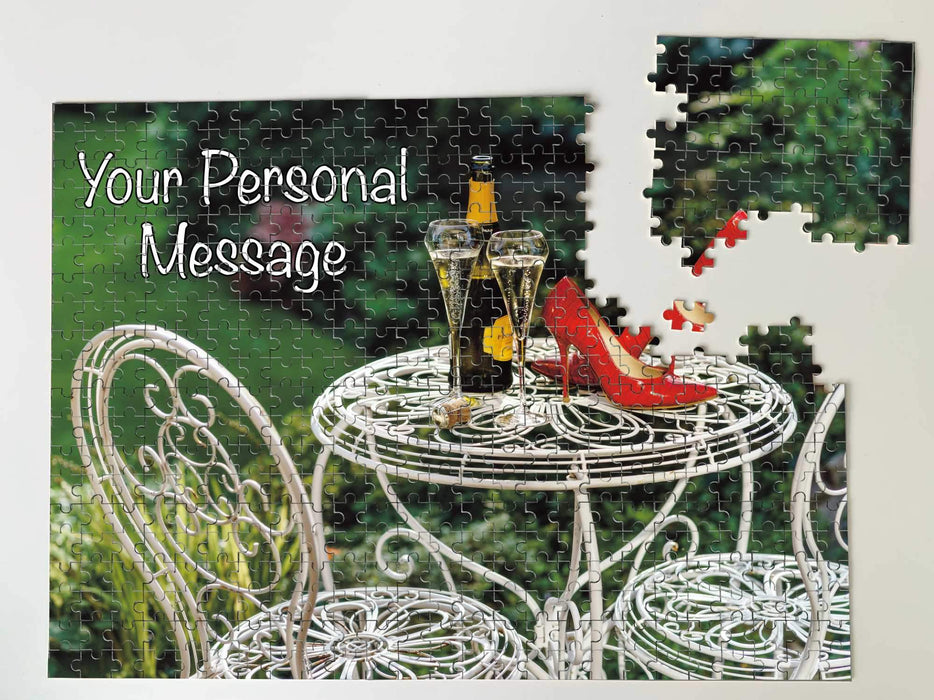 A jigsaw puzzle seen from overhead, on the jigsaw there is an image on the box of a pair of red high heel shoes sat on a garden table with a bottle of fizzy wine, along with a personal message, the jigsaw is broken
