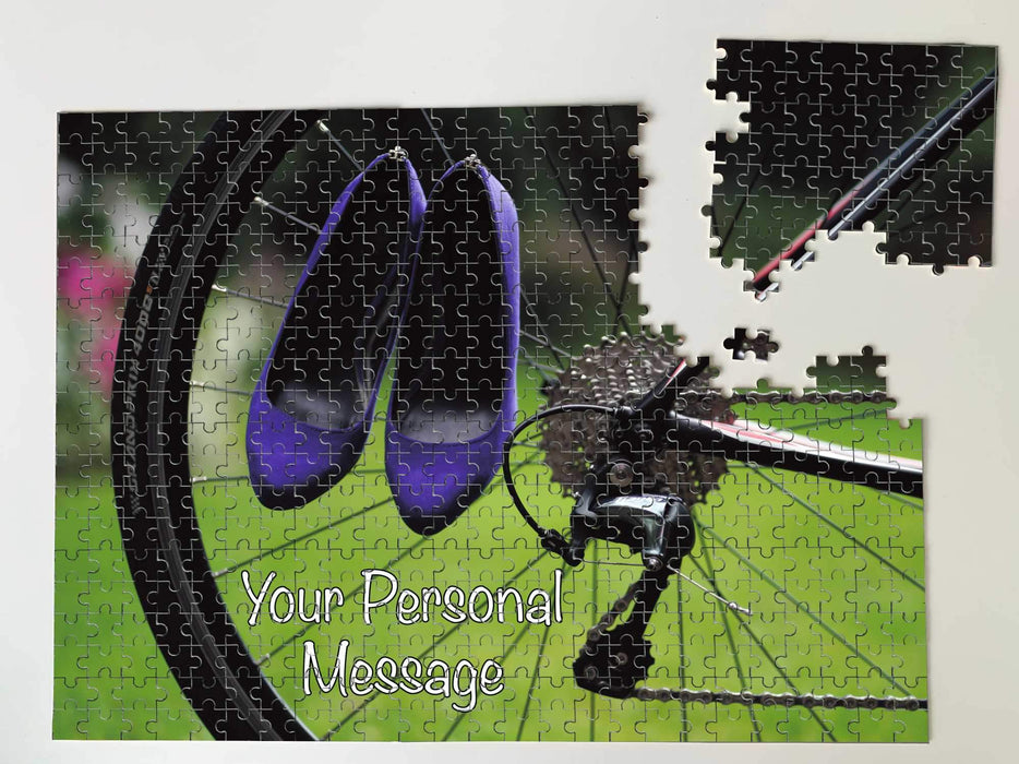 A jigsaw seen from the top, the jigsaw having an image of a pair of purple high heel shoes hung on the rear wheel of a road bike, along with a personal message, the jigsaw is slightly broken up