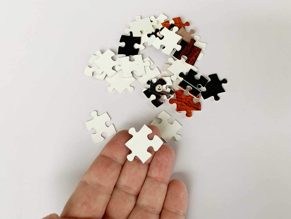 An open hand with a jigsaw piece resting on the finger, there are other jigsaw pieces laying adjacent to the hand