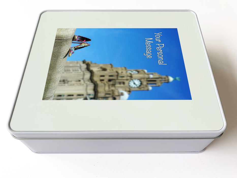 A white tin box with an image of a pair of shoes on a wall in front of the liverpool liver building