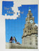 A jigsaw with an image the liverpool liver building with a pair of shoes on a wall in the foreground, with the jigsaw partially broken