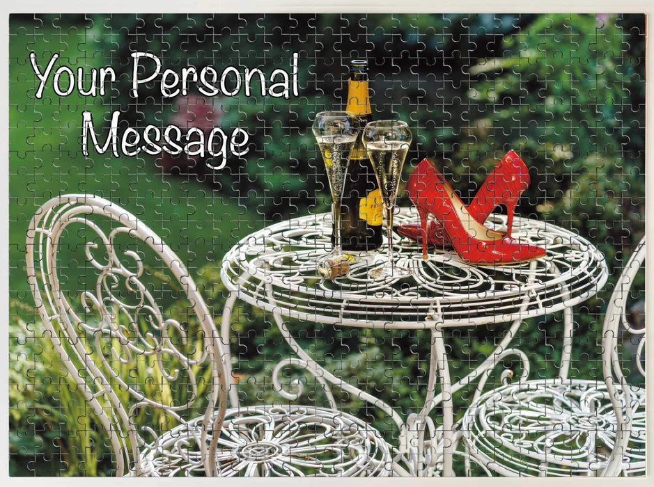 A jigsaw puzzle seen from overhead, on the jigsaw there is an image on the box of a pair of red high heel shoes sat on a garden table with a bottle of fizzy wine, along with a personal message
