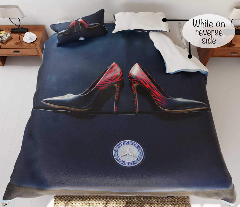 A duvet on a bed, the duvet having an image of a pair of shoes on the bonet of a dark blue high performance car, part of the duvet is folded back to show a white underside