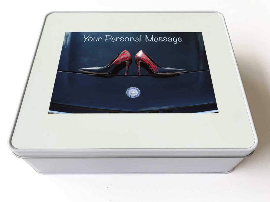 A white tin box with a photo on the lid, the photo is an image of a pair of blue high heel shoes on the bonnet of a high performance car, along with a printed personal message