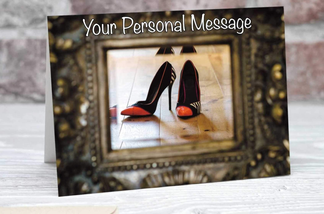 A greetings or birthday card showing a mirror, the mirror surrounded by a brass mount, an in the mirror is a reflection of a pair of orange high heel shoes along with a personal message
