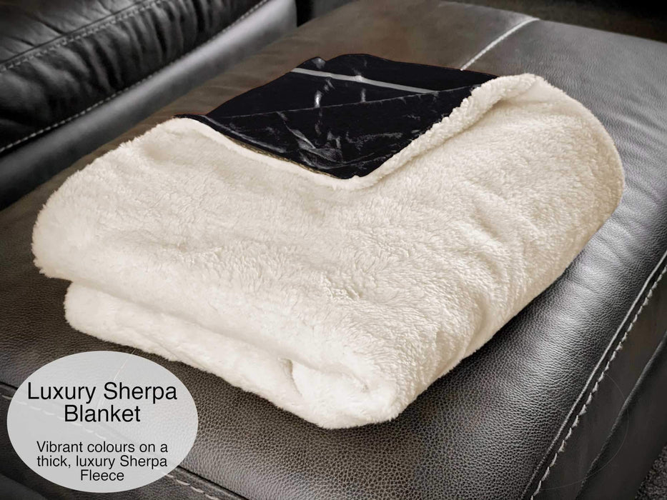 A thick sherpa blanket folded over and sat on a couch, a corner is folded back to show that the other side of the blanket is black