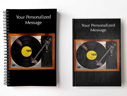 A pair of notebooks side by side, both with an image of a record player with a black, and blue triangle, labelled vinyl record playing, with a personal message printed