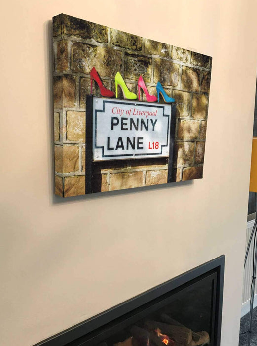 canvas print of famous penny lane street sign with four ladies shoes on top of the sign, the canvas print hung on a chimney above a lit fire, the whole thing seen from side on position to the left