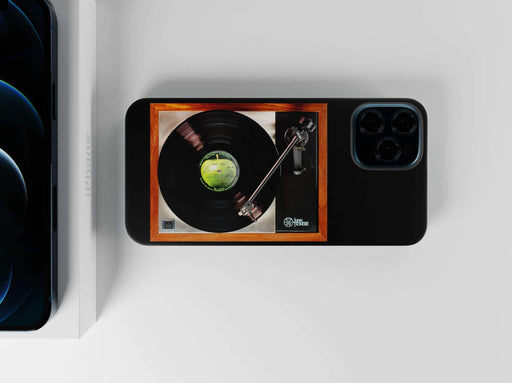 a mobile phone case with the image of a record player a vinyl record playing, sporting a label with a green apple, all adjacent to a box with an iphone showing