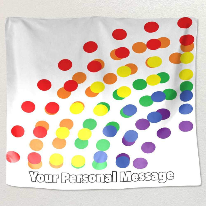 A tapestry hung on a white wall, the tapestry has a series of polka dots on it, the polka dots coloured with a rainbow colour on a white background, along with a personal message printed