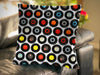 A cushion sat on a couch, the cushion decorated with an image of vinyl records arranged in a mosaic pattern, on a white background