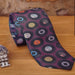 A rolled neck tie on a wooden surface, the tie being burgundy in colour and having coloured vinyl records on it