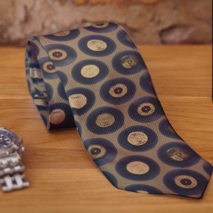 A rolled neck tie on a wooden surface, the tie being gold in colour and having gold coloured vinyl records on it