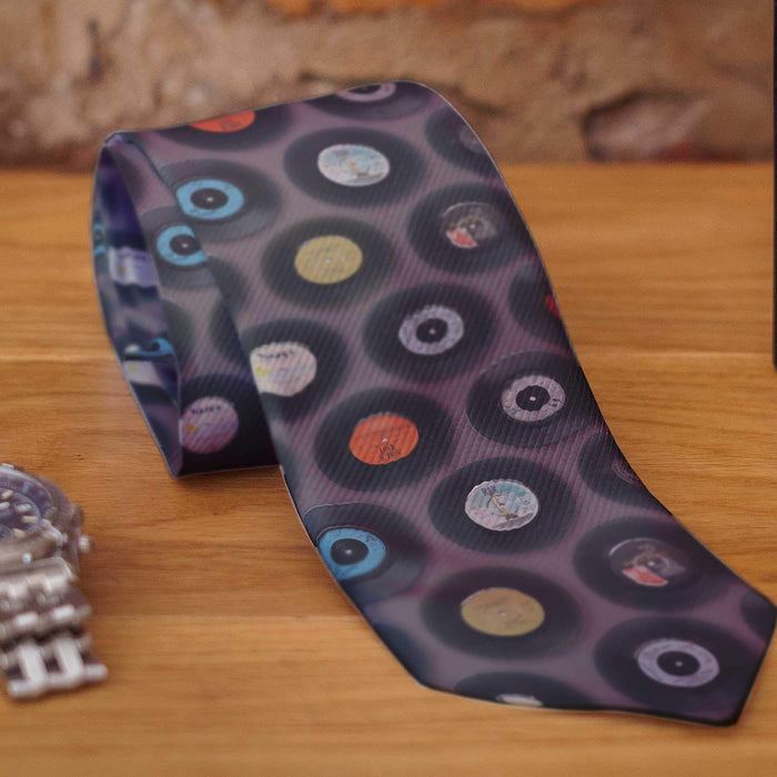 A rolled neck tie on a wooden surface, the tie being grey in colour and having coloured vinyl records on it