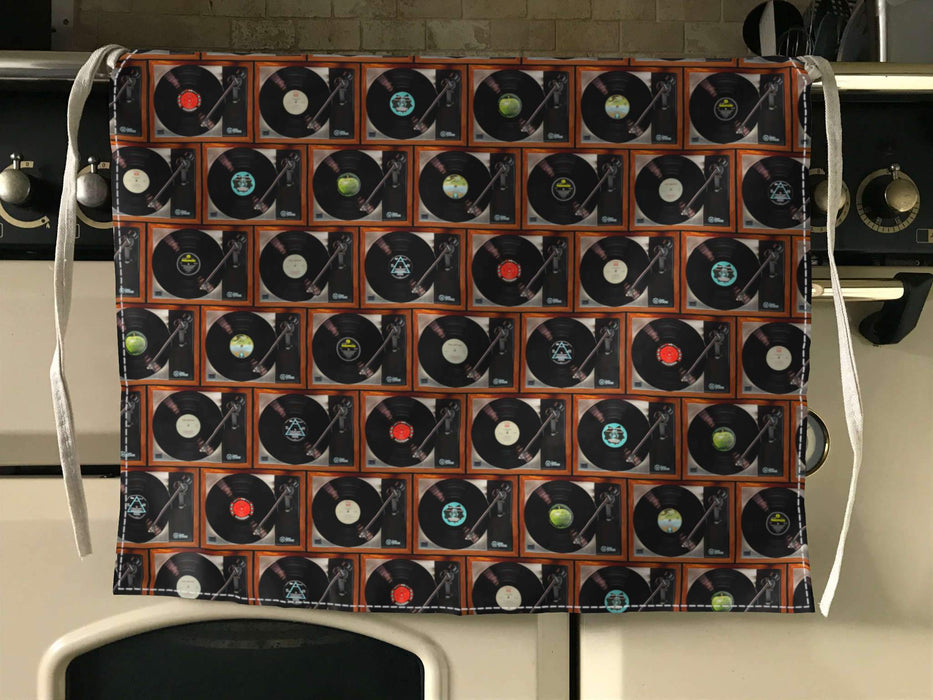 an apron folded over a kitchen cooker, the apron having a mosaic pattern of record players with a mixture of vinyl records