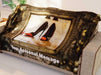 A blanket draped over a couch, the blanket having an image of a pair of black and orange high heel shoes reflected in a brass mirror, along with a printed personal message