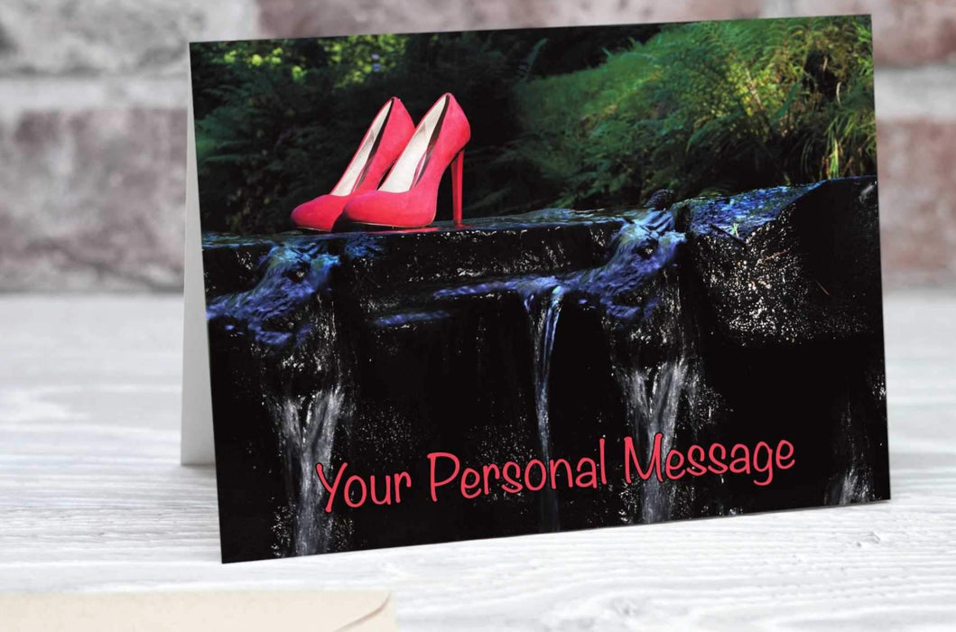 A greetings or birthday card showing a pair of pink high heel shoes on a rock half way across a flowing river, there is a personal message on the card
