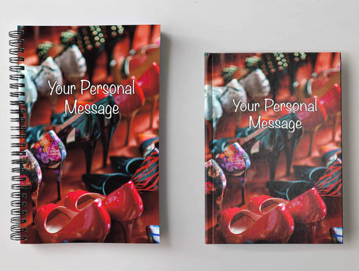 Two notebooks, side by side, both having covers with an image of a large quantity of high heeled shoes all lined up adjacent to each other in multiple rows along with a personal message on the cover