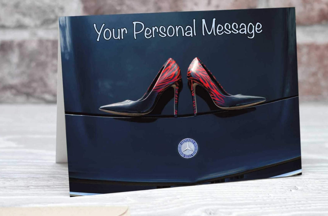 A pair of shoes on the bonnet or hood of a dark purple car, the logo of the car being visible below the shoes, the image is seen from above, and there is a personal message on the card