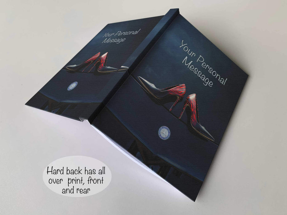 An open hardback notebook with a  cover of an image of a pair of dark blue ladies high heel shoes laid flat on the bonnet or hood of a high performance car, with a personal message on the cover